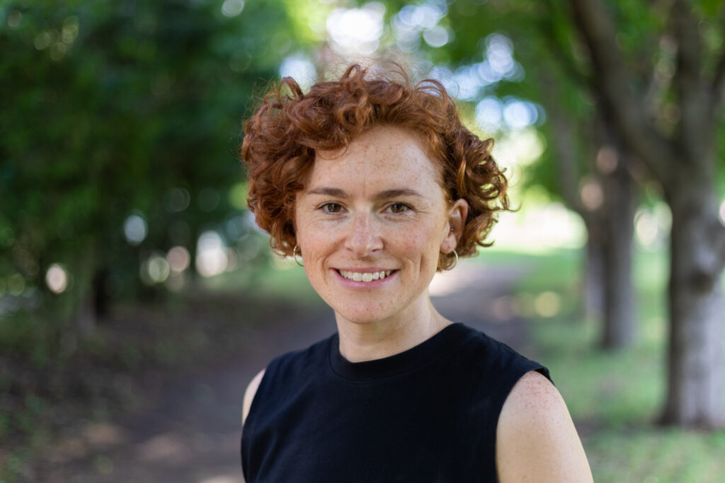 Headshot of Caitlin, a woman with red curly hair standing in a park